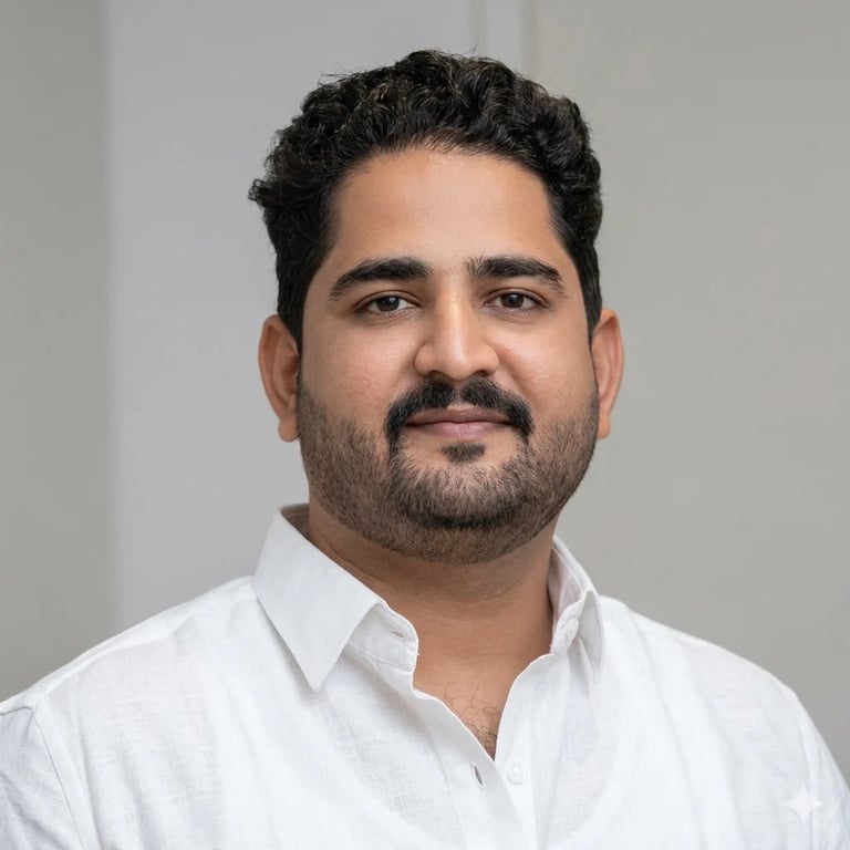 Professional headshot of a man with dark curly hair and beard wearing a white button-up shirt against a neutral gray background